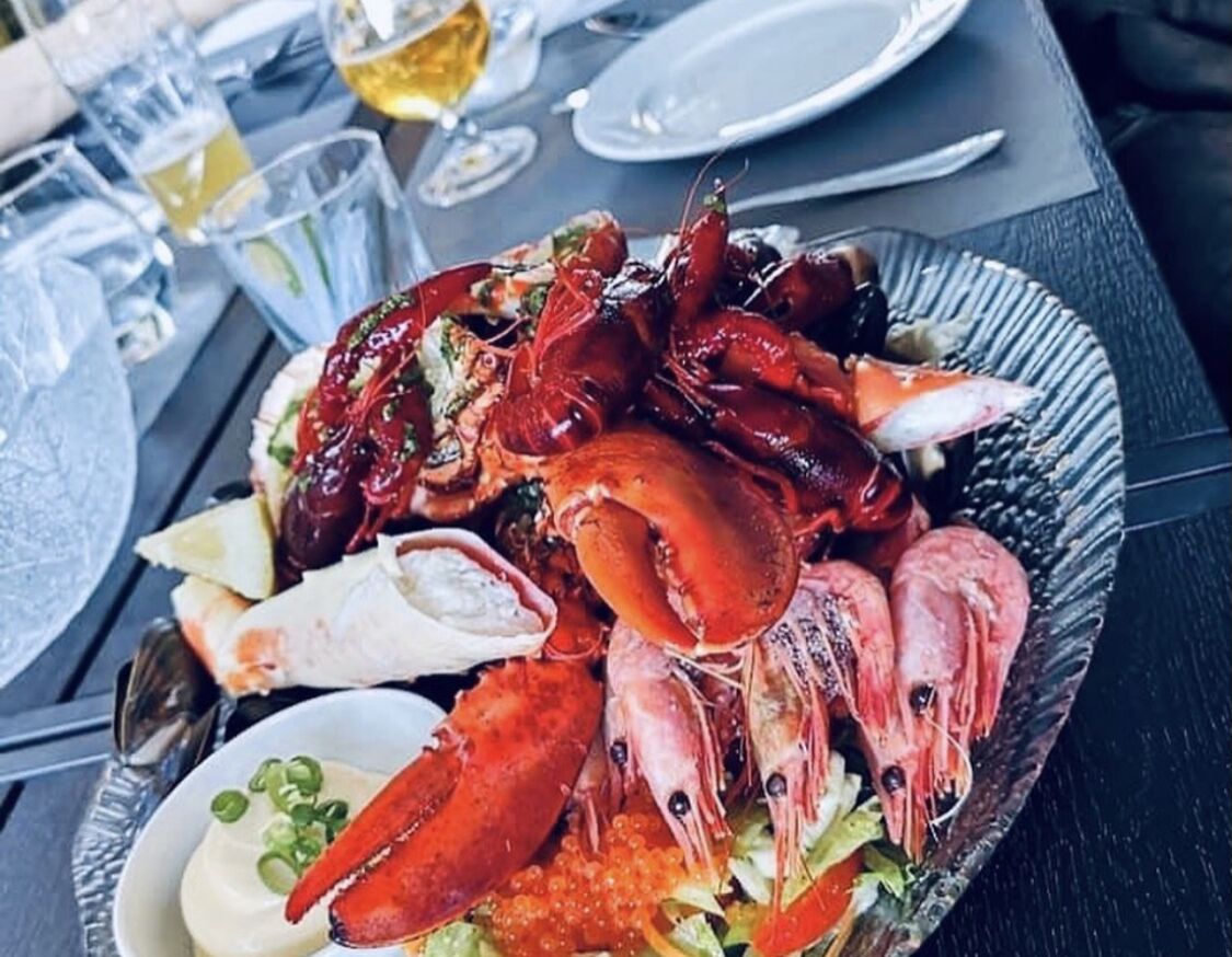A seafood platter with various types of shellfish on a plate, accompanied by a small bowl of sauce and some lemon wedges.