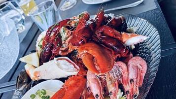 A seafood platter with various types of shellfish on a plate, accompanied by a small bowl of sauce and some lemon wedges.