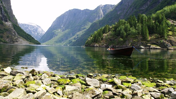 Un bateau sur une rivière paisible, bordée de rives rocheuses et entourée de montagnes escarpées.