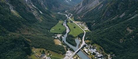 An aerial view of a valley with a river, a bridge, and a small settlement with buildings and a marina.