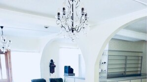 Un vaste espace de vie agrémenté de meubles en osier, d’un lustre et offrant une vue sur la cuisine.
