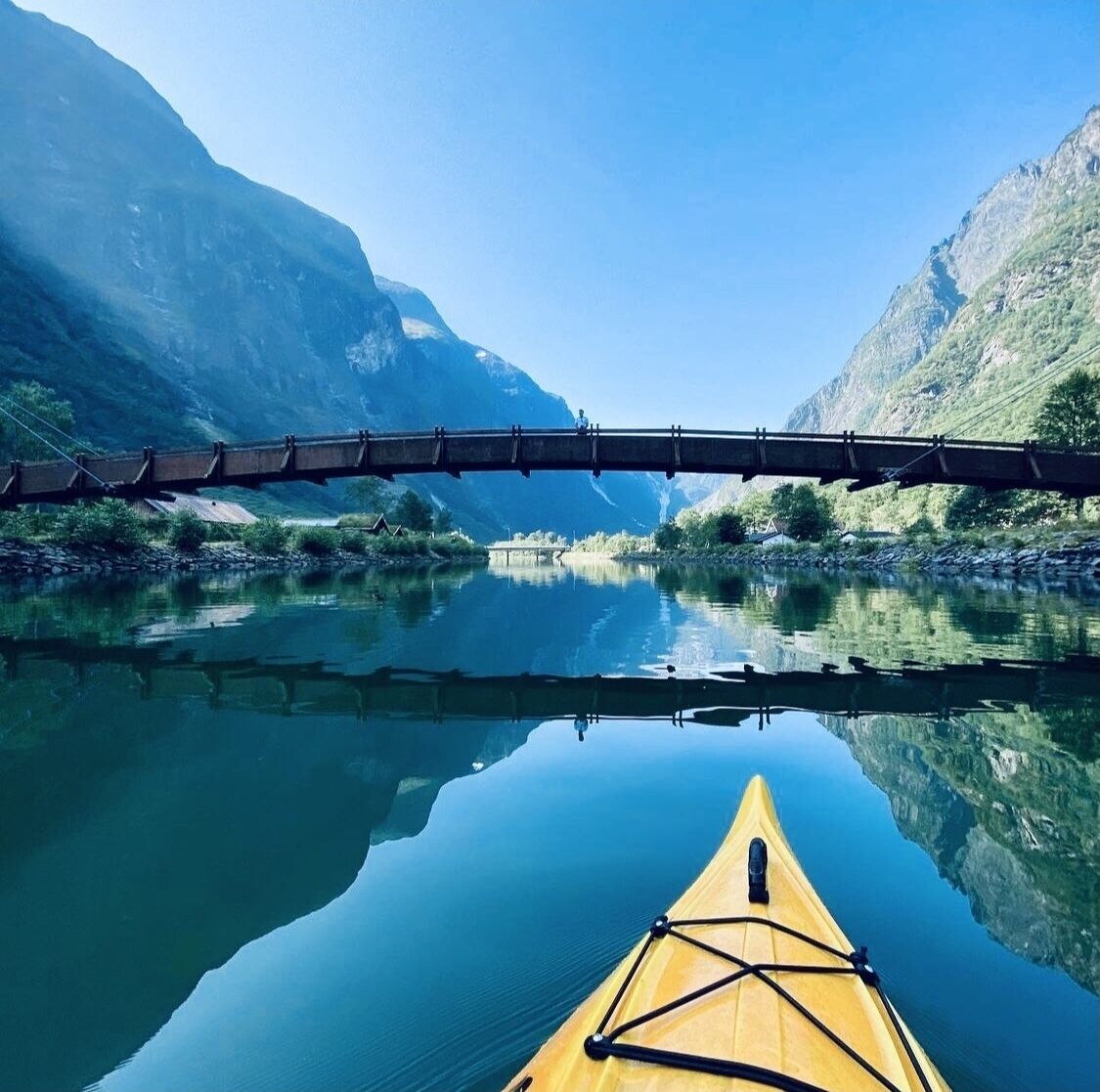 A yellow kayak on a calm river with a bridge in the background.