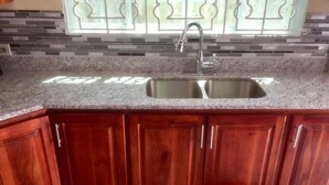 Eine Küche mit Granit Arbeitsplatte, doppelter Spüle, Holzschränken und einem gemusterten Teppich.