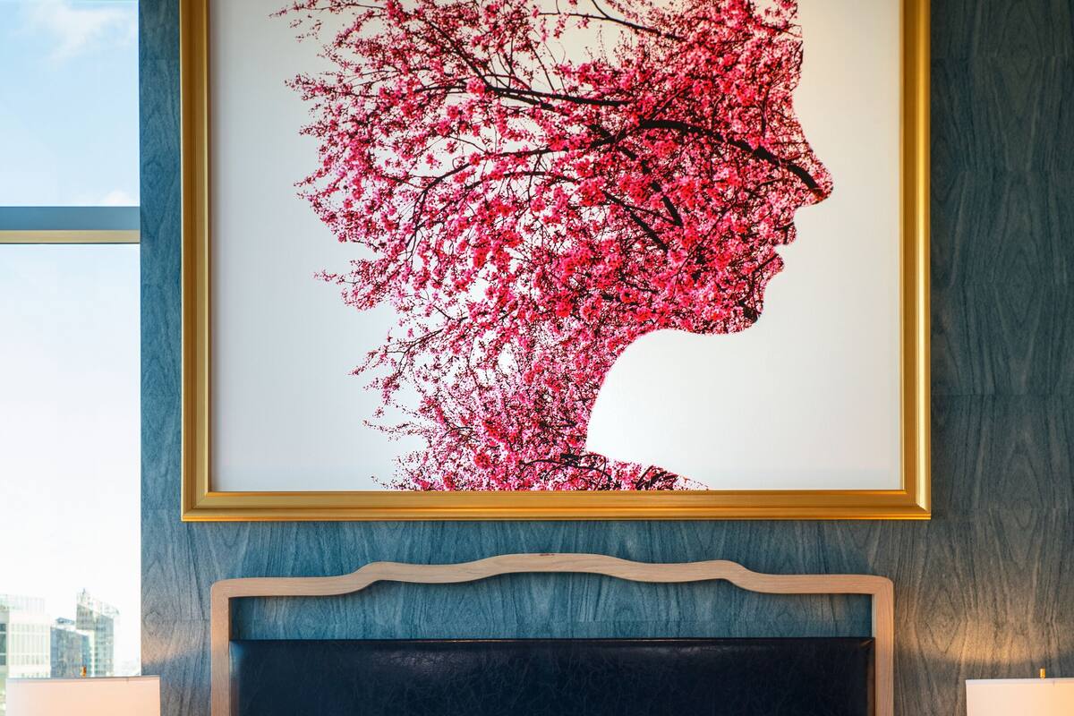 A hotel room with a large bed, a headboard, and a framed artwork above the bed.