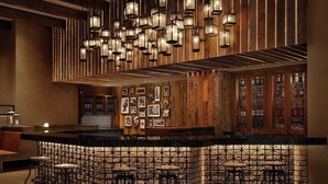 A bar area with a wooden bar counter, multiple hanging lantern-style lights, and a stone wall backdrop.
