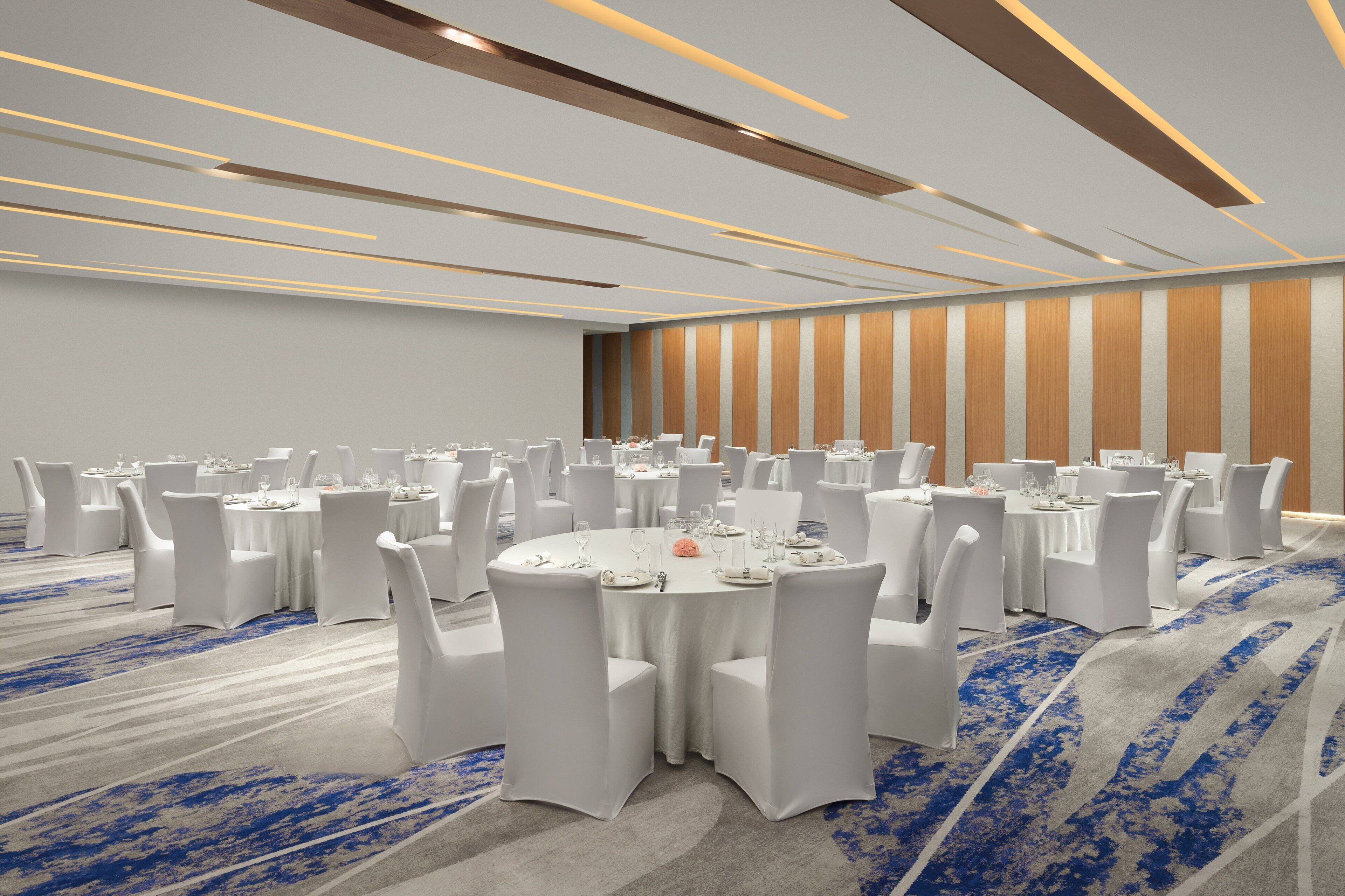 Uma grande sala de conferências com várias mesas redondas, cada uma com cadeiras brancas e louças postas.
