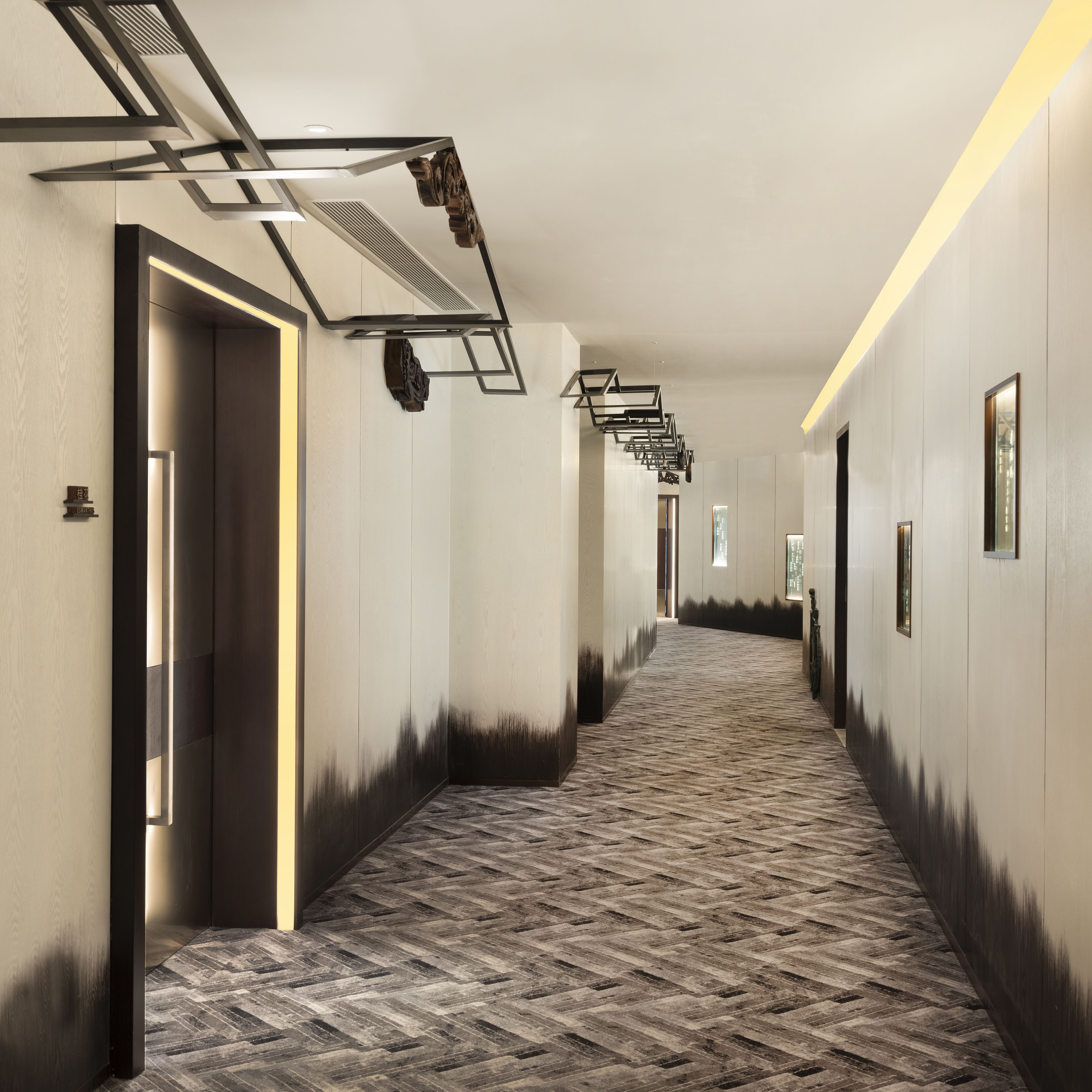 A hotel corridor with a herringbone patterned floor, recessed lighting, and a modern ceiling design.