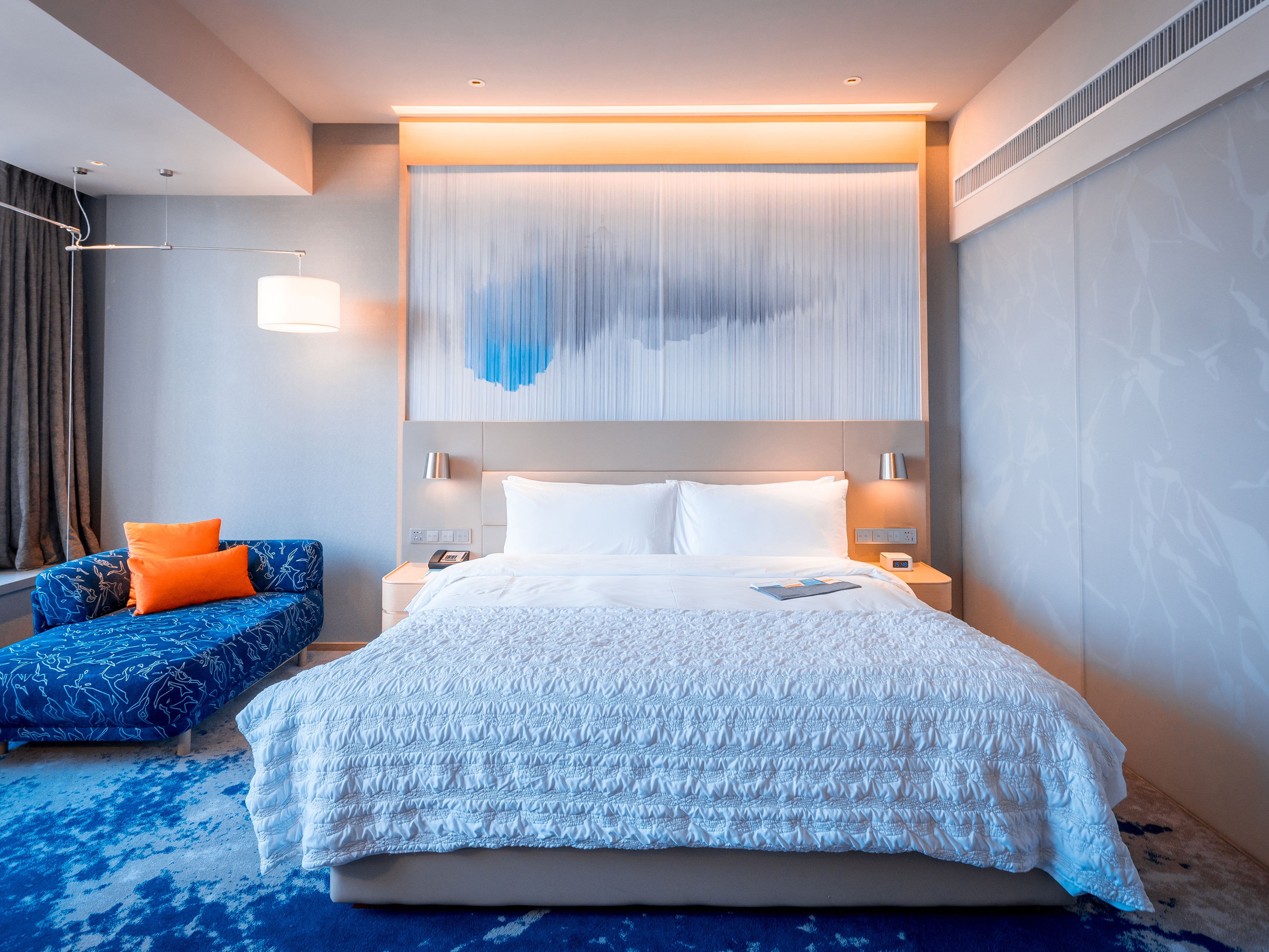A modern hotel room with a large bed, a sofa, and a wall-mounted artwork.