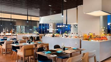 A modern restaurant with wooden flooring, blue chairs, and a central island with food and drinks.
