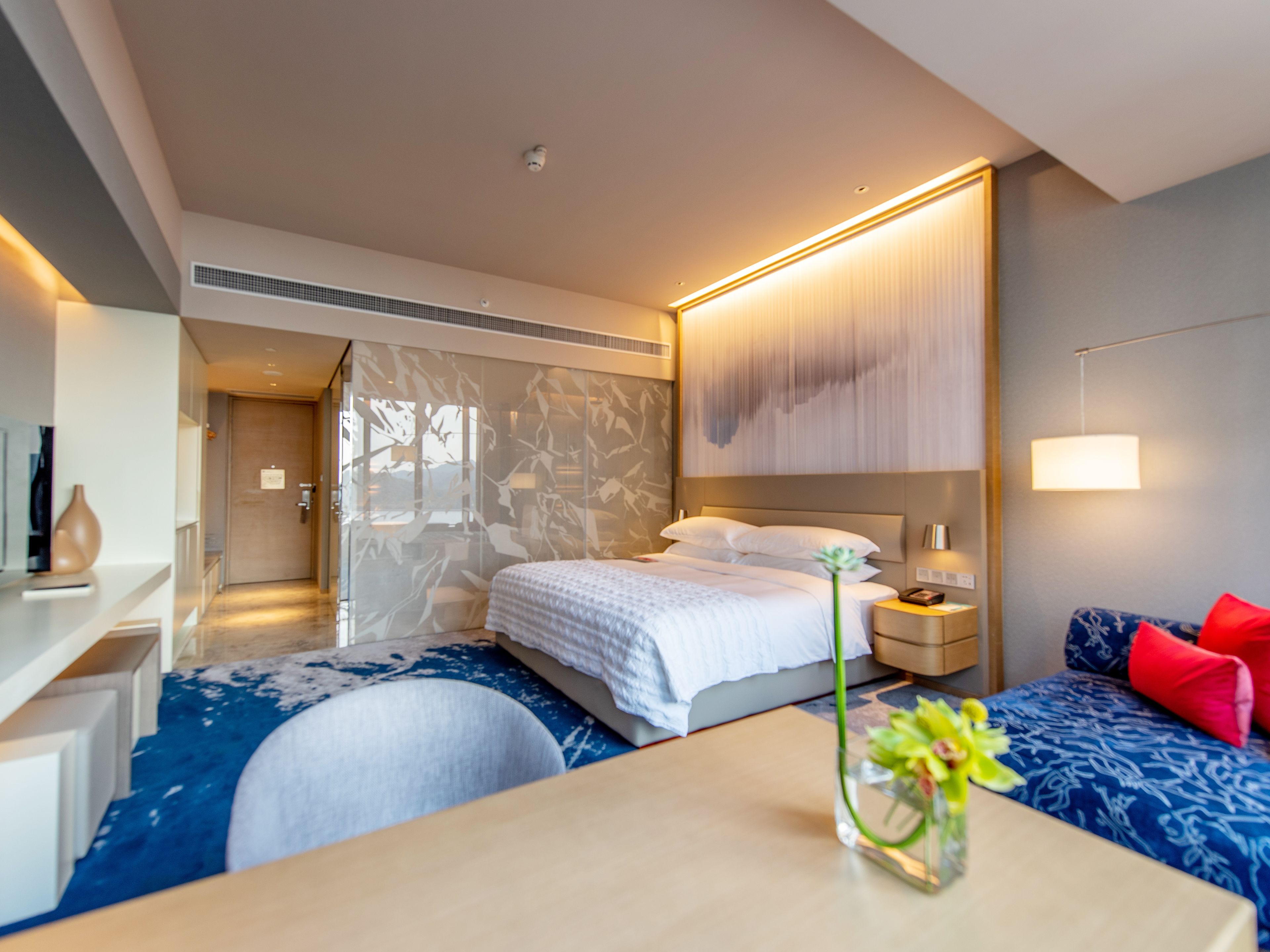 Ein modernes Hotelzimmer mit Bett, Nachttisch und Schreibtisch mit Blumenvase.