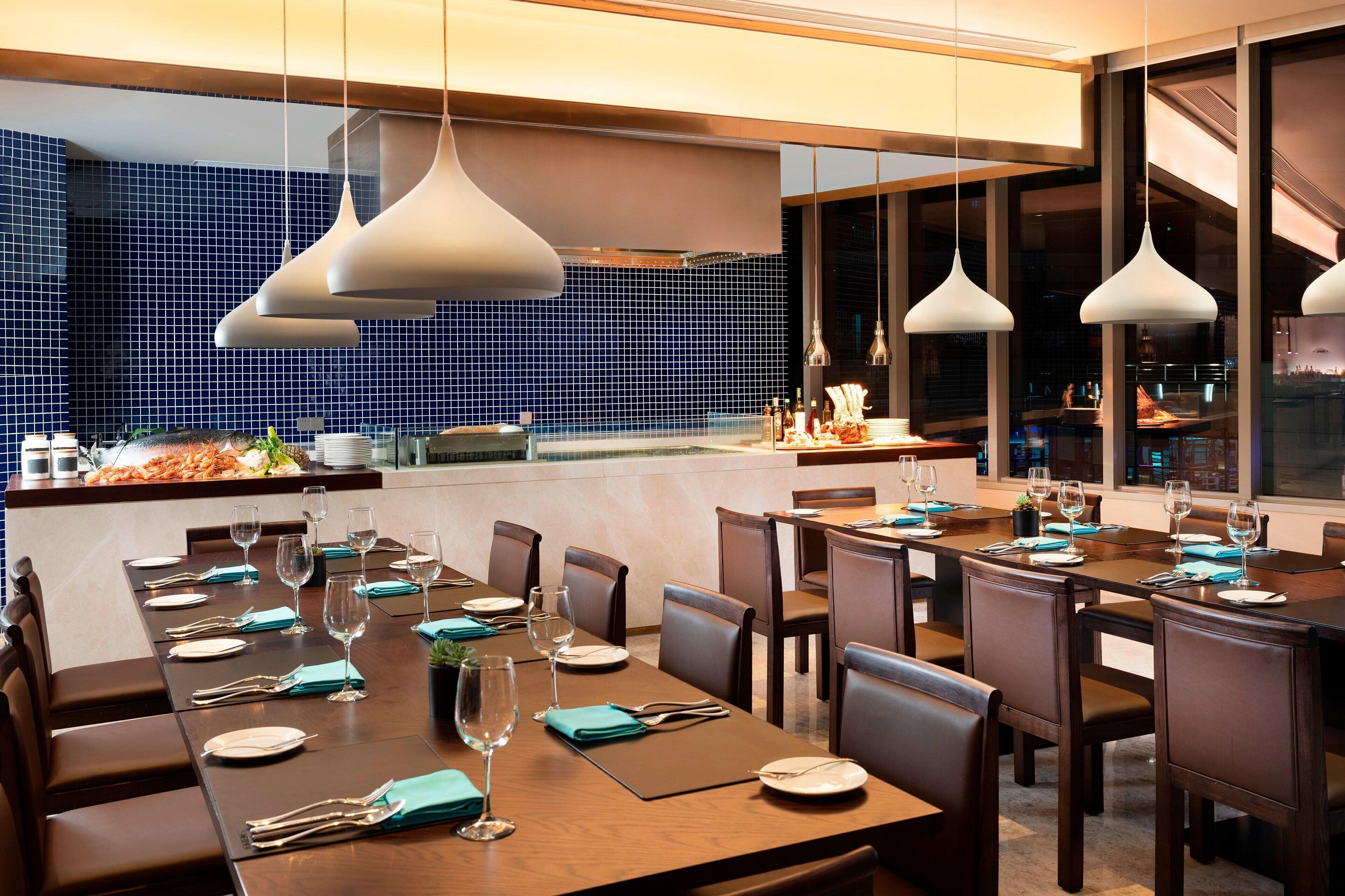 Ein Restaurant mit mehreren Tischen für Gäste, einer Küchenzeile und großen Fenstern mit Blick auf die Stadt.