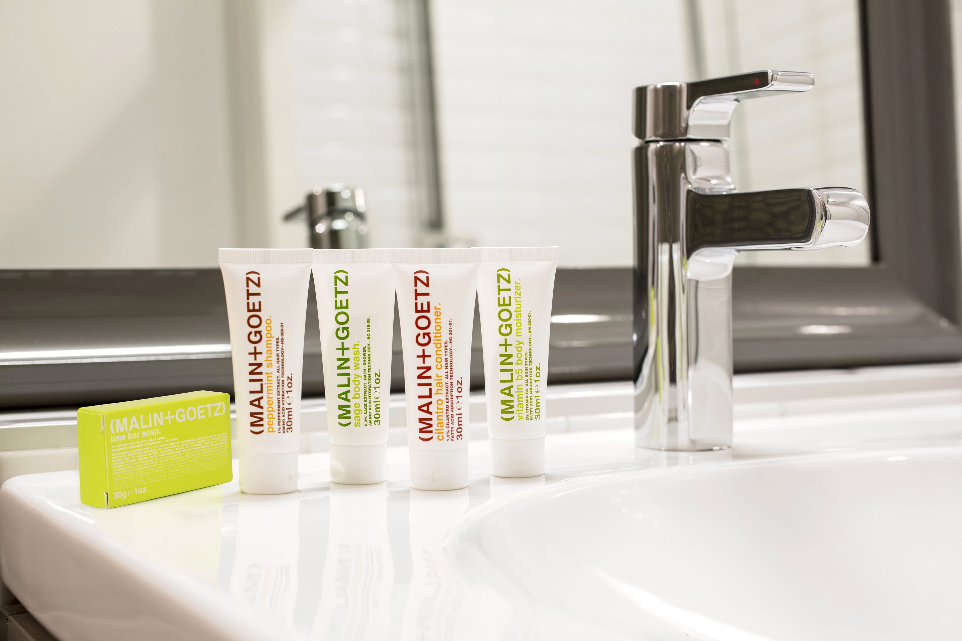 A bathroom sink with four bottles of MALIN+GOETZ hair care products and a lime bar soap.