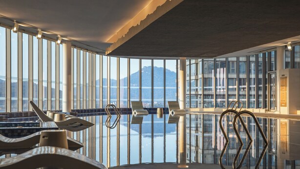 A modern indoor swimming pool with large windows, a view of a mountain, and a poolside lounge area. - Le Méridien Hangzhou, Binjiang (Hangzhou)