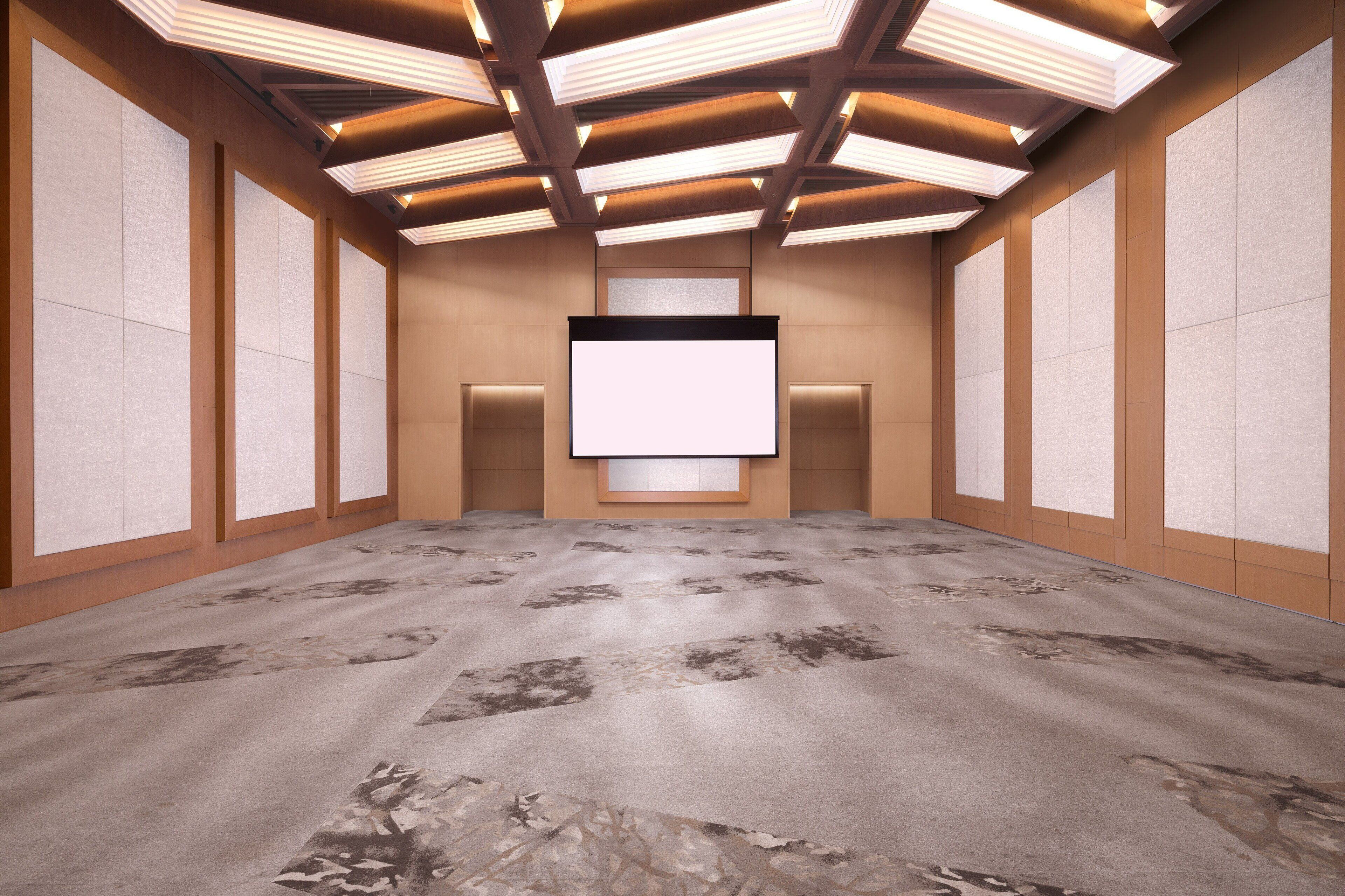 A conference room with a large screen, wooden panel walls, and a patterned carpet.