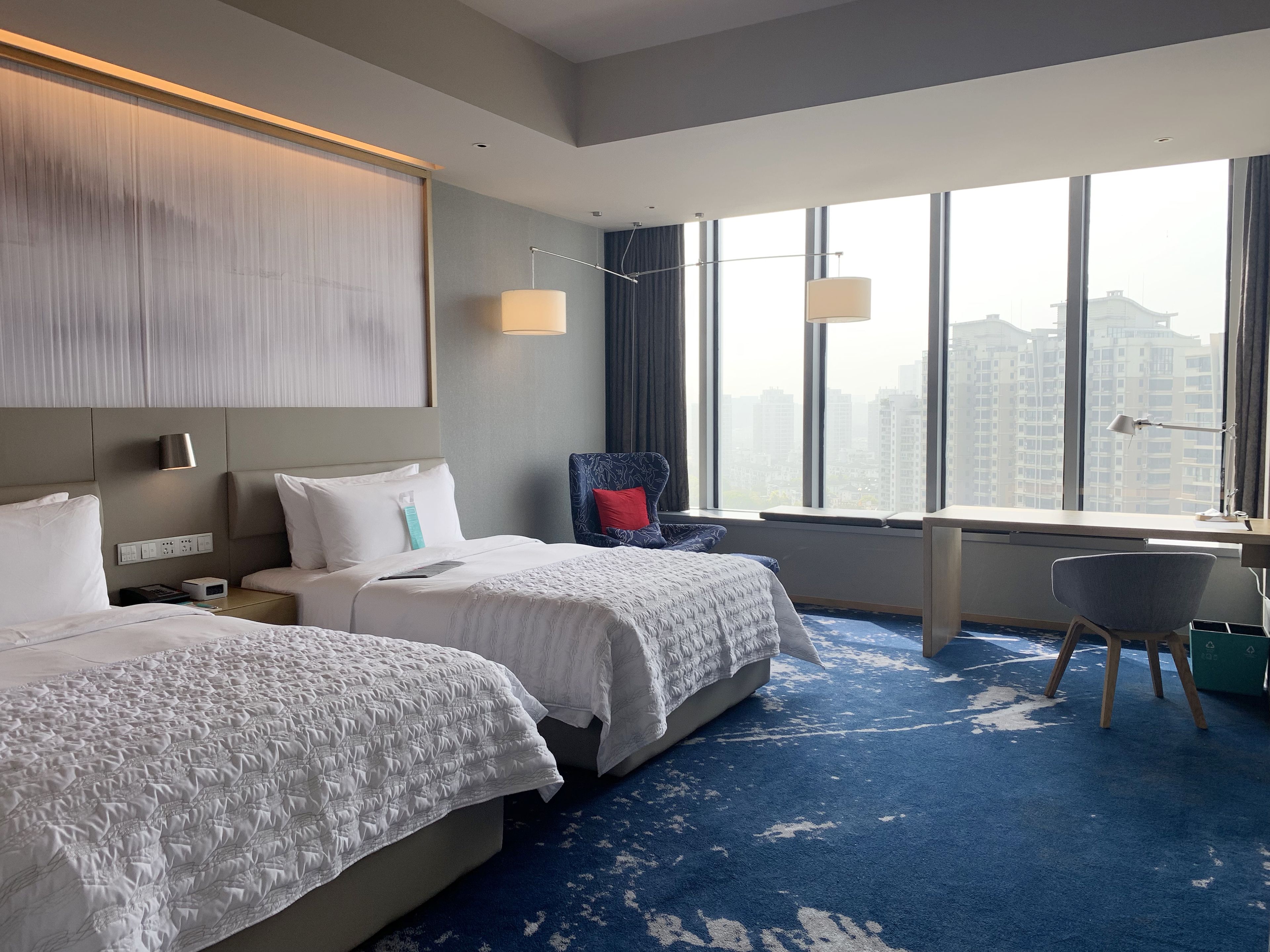 Une chambre d’hôtel avec deux lits, un bureau, une chaise et une grande fenêtre donnant sur la ville.
