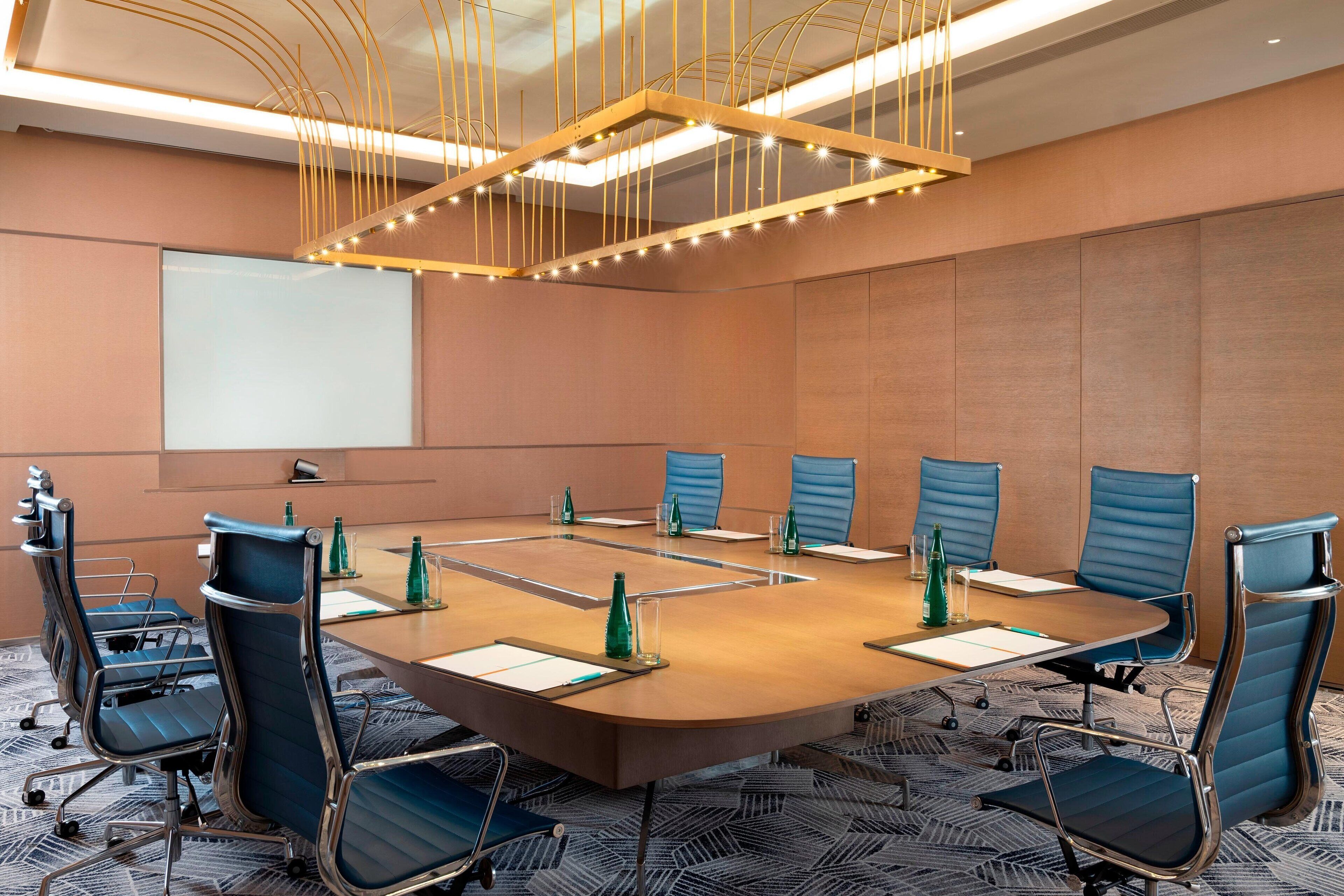 Une salle de conférence équipée d’une grande table ovale, de six chaises bleues et d’un écran de projection.