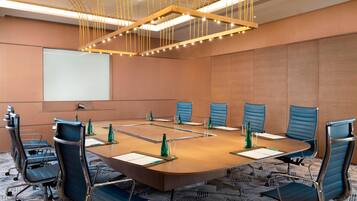 Une salle de conférence équipée d’une grande table ovale, de six chaises bleues et d’un écran de projection.