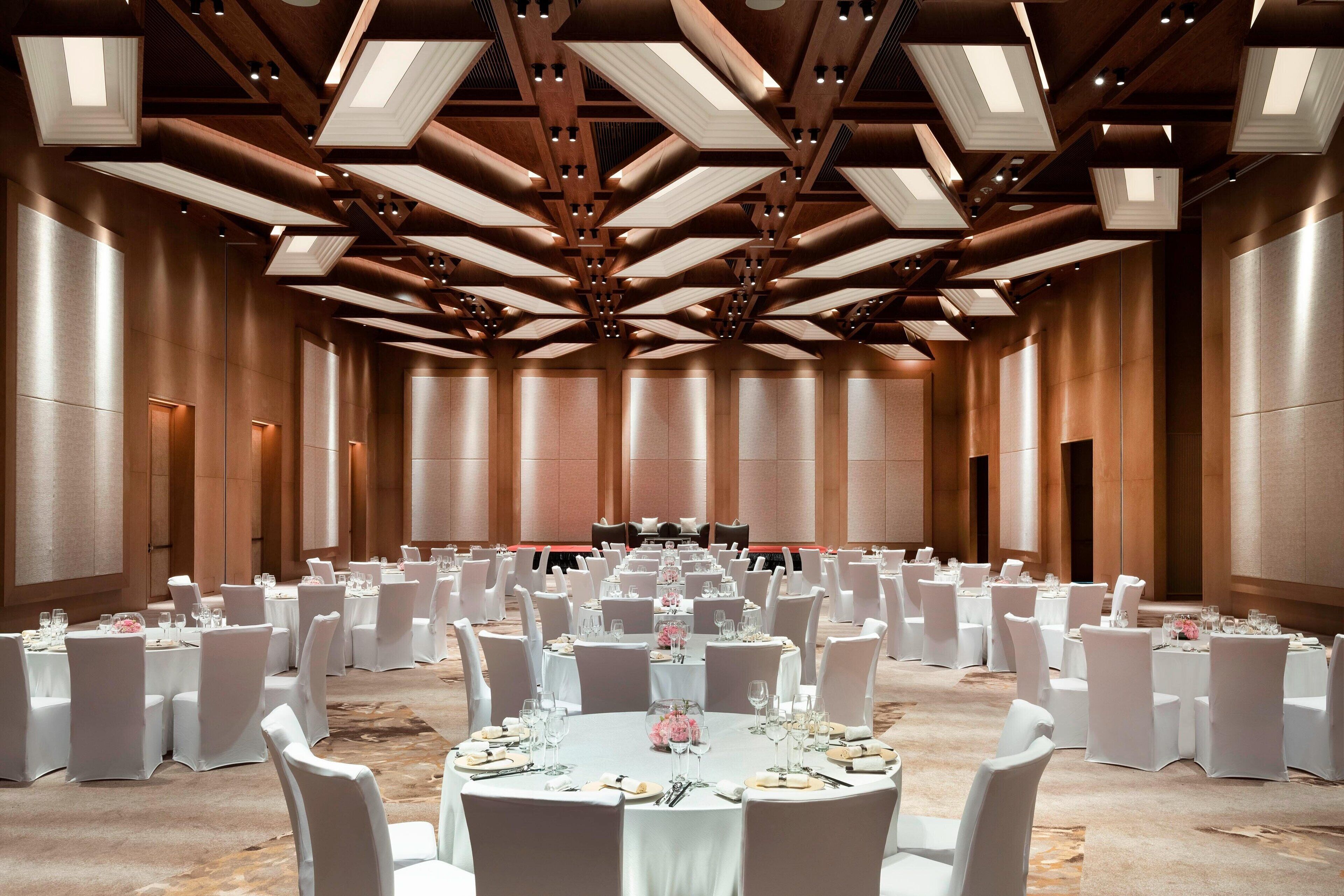 A large conference room with round tables, white chairs, and a high ceiling with exposed beams.