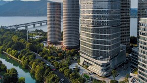 A modern high-rise building complex with a glass facade, surrounded by greenery and a river. - Le Méridien Hangzhou, Binjiang (Hangzhou)