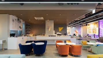 A modern hotel lobby with a reception desk, seating areas, and a bar.