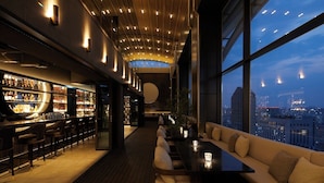 Een moderne bar met uitzicht over de stad, houten vloeren en een zithoek met kussens.