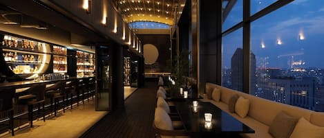 Un bar moderno con vistas a la ciudad, suelo de madera y una zona de estar con cojines.