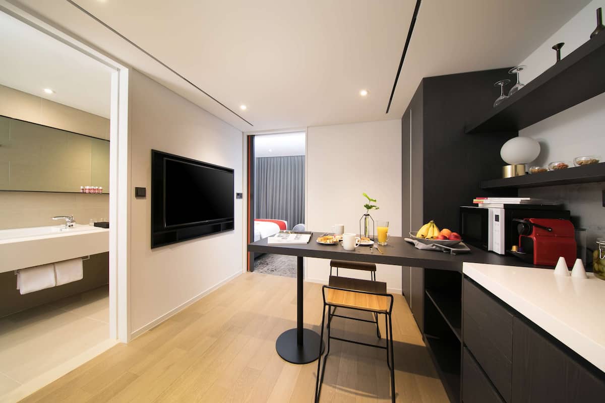Une chambre d’hôtel moderne équipée d’une télévision à écran plat, d’un coin repas avec une table mise pour le petit-déjeuner, d’un four à micro-ondes et d’une machine à café.