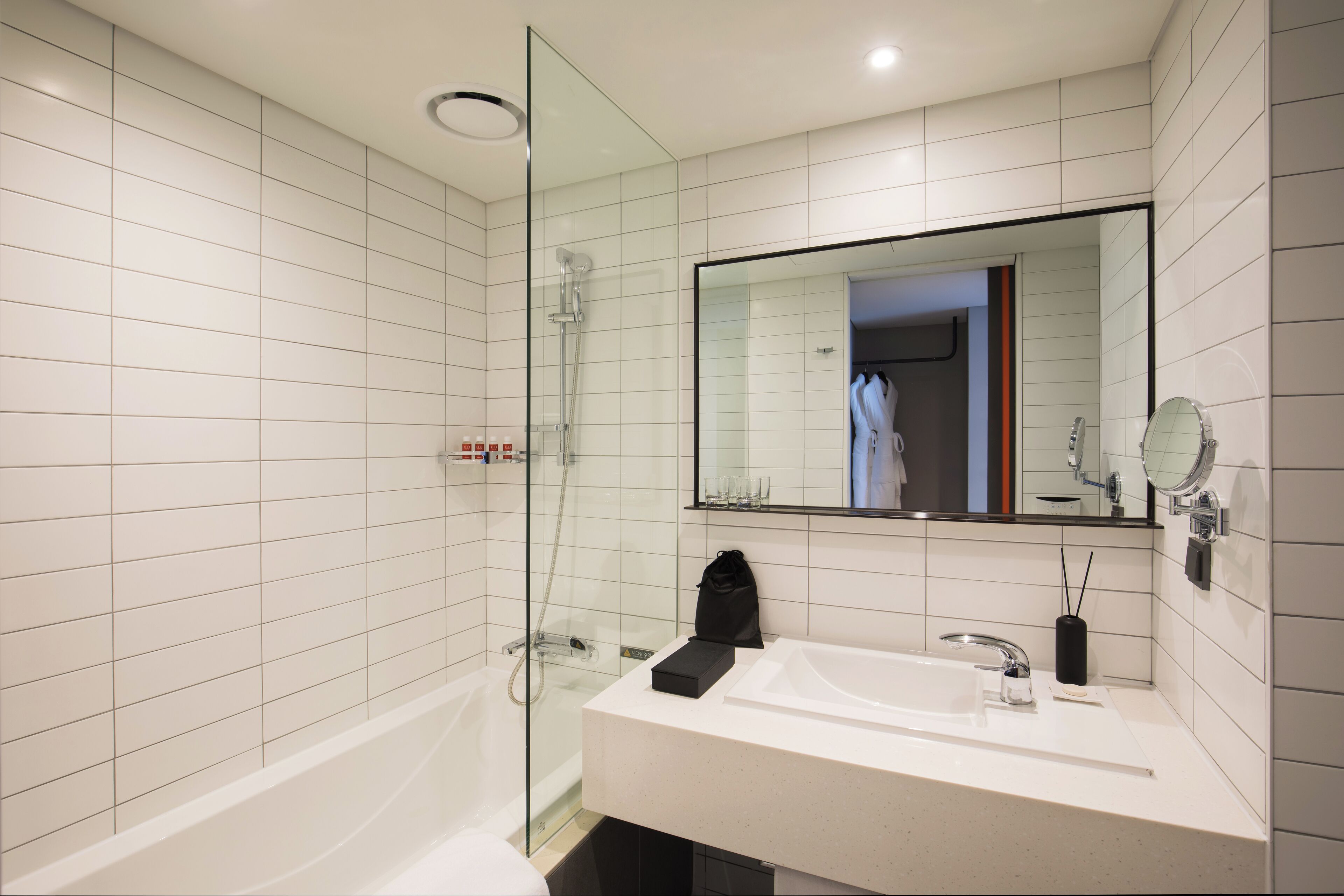 Un baño moderno con ducha envuelta en vidrio, un espejo grande y un lavabo blanco.