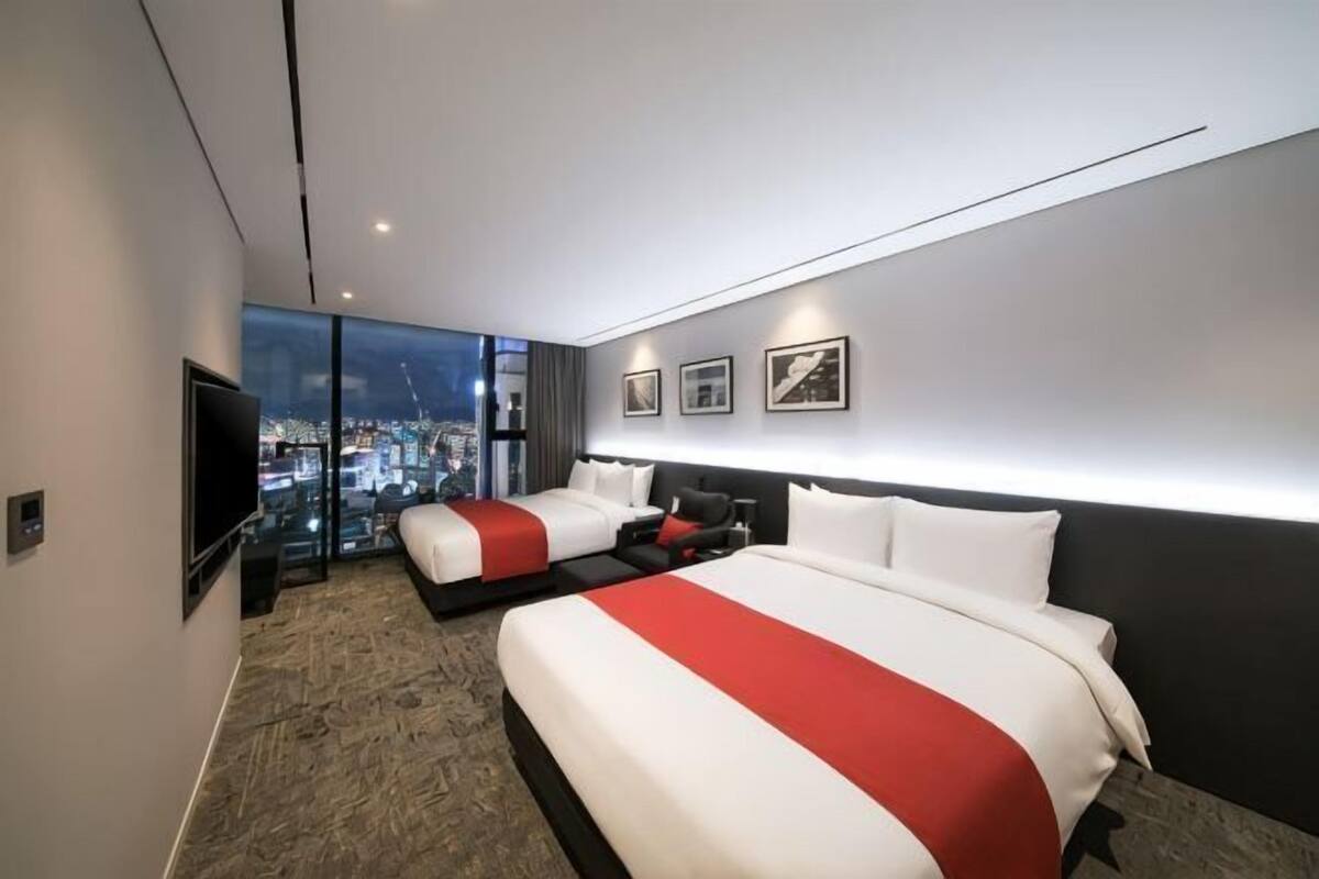 Une chambre d’hôtel moderne avec deux lits, une grande fenêtre, un téléviseur à écran plat et des œuvres d’art accrochées au mur.