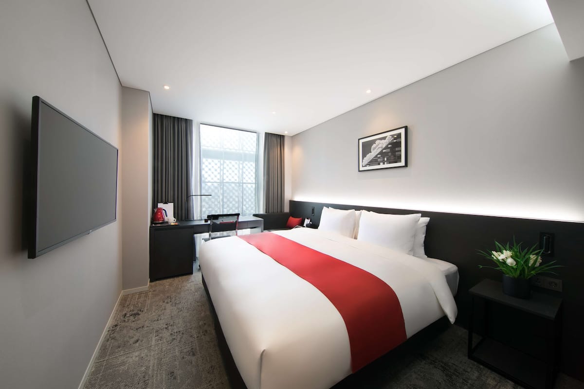 Une chambre d’hôtel moderne dotée d’un grand lit, d’un téléviseur à écran plat, d’un bureau et d’une fenêtre avec des rideaux.