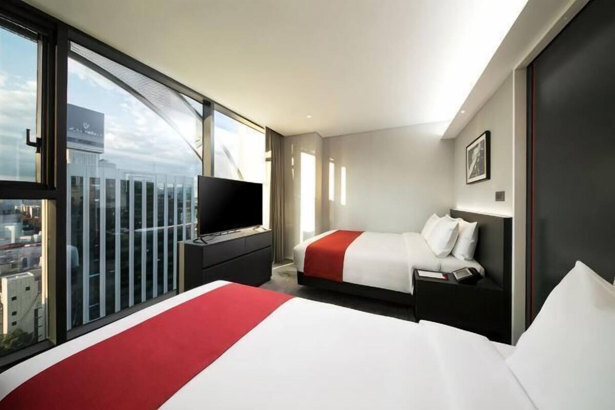 Une chambre d’hôtel avec un grand lit, un téléviseur posé sur un meuble, une fenêtre donnant sur la ville et un balcon.