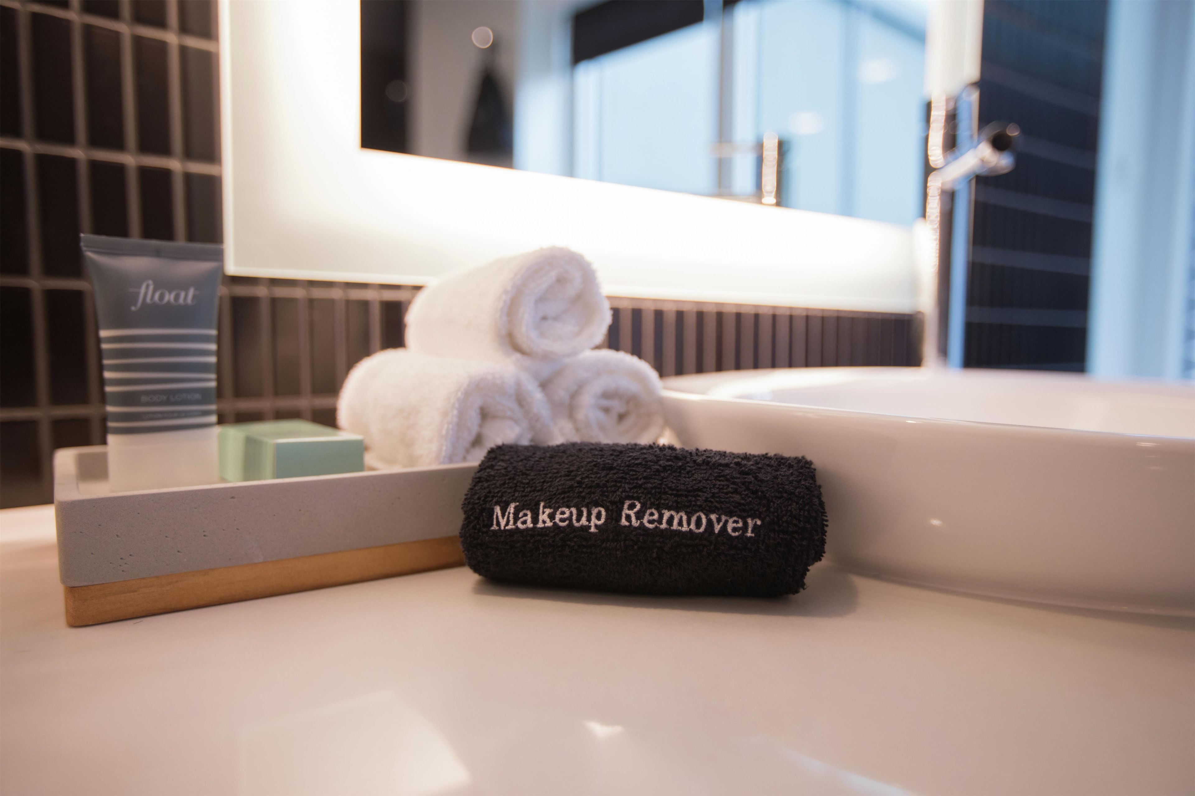 Un baño con lavamanos, espejo, toalla y neceser de maquillaje.