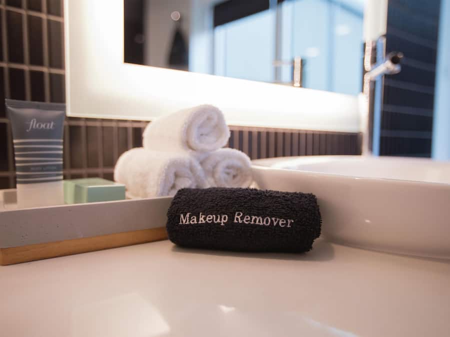 A bathroom with a sink, a mirror, a towel, and a makeup remover pouch.