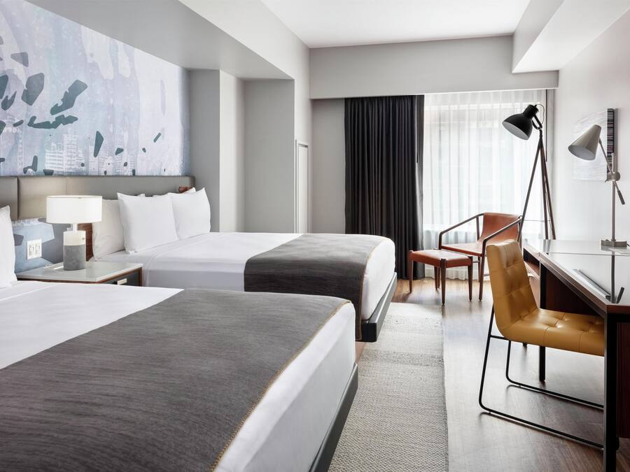 Habitación de hotel con dos camas, un escritorio, una silla, una lámpara y un cuadro abstracto grande en la pared.