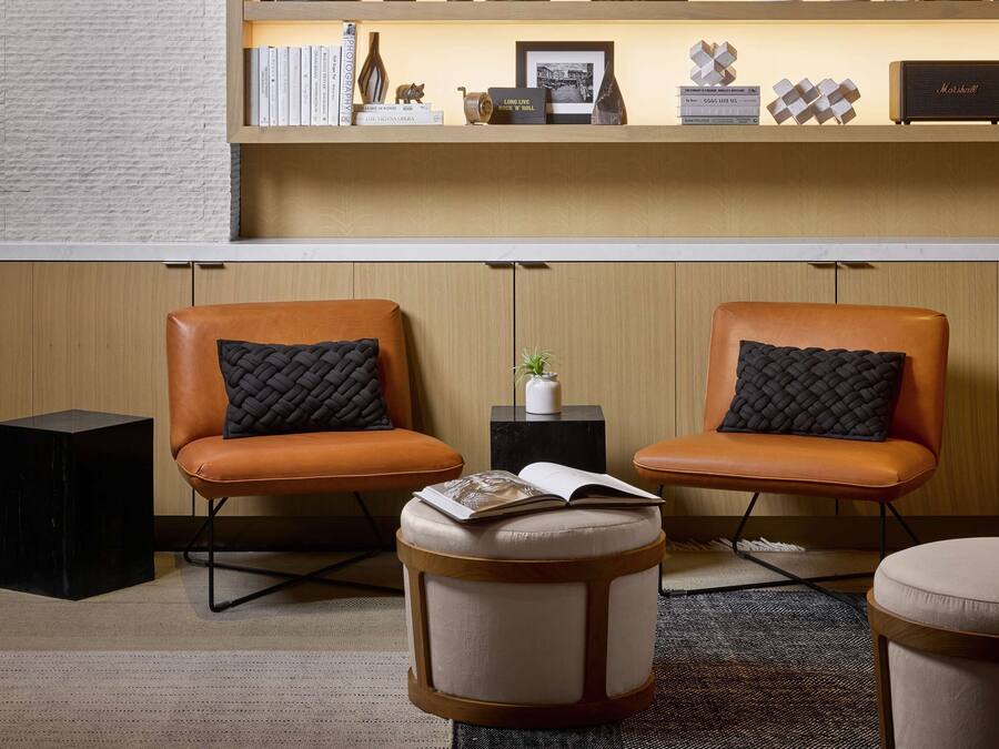 Una sala de estar moderna con una estantería de madera, dos sillones de cuero y un otoman redondo.