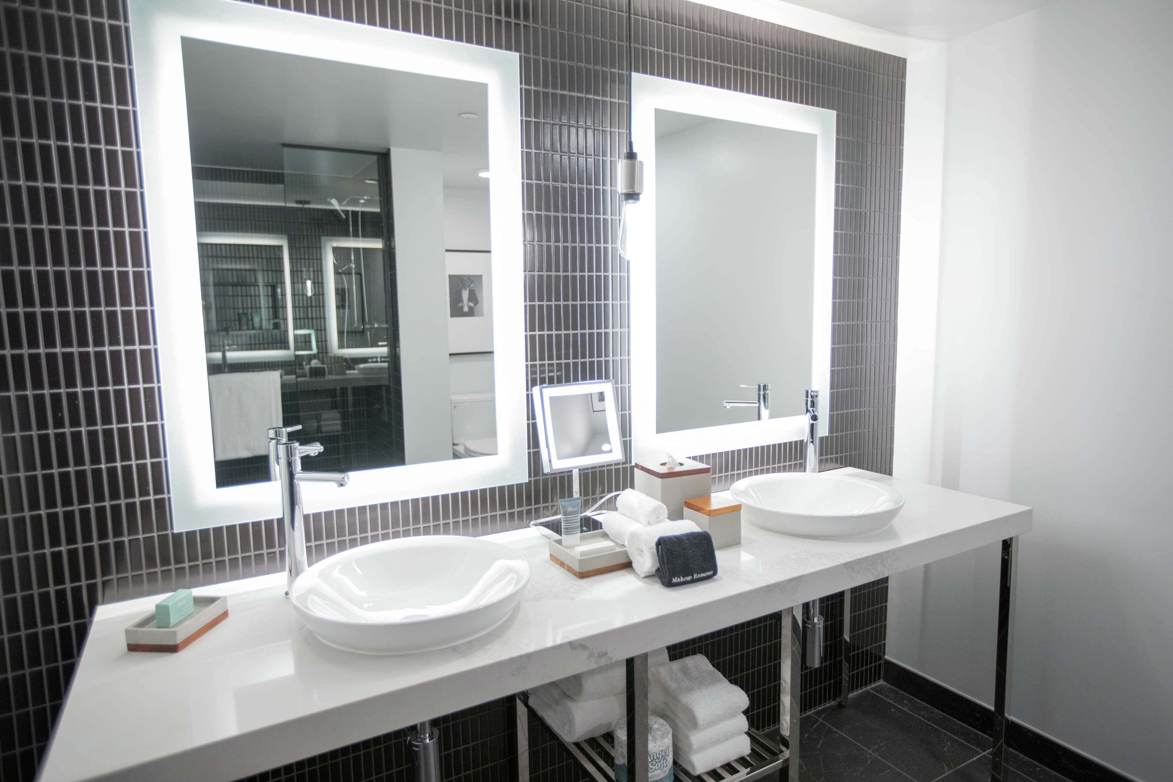 Een moderne badkamer met twee wastafels, grote spiegels en een betegelde spatwand.