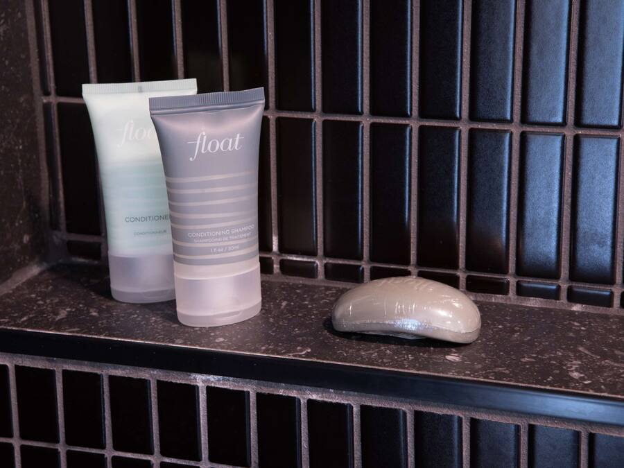 Une étagère de salle de bain avec trois flacons de produits de toilette étiquetés « flottant » et un savon.