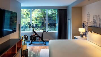 A hotel room with a large bed, a TV, an exercise bike, and a cityscape mural.