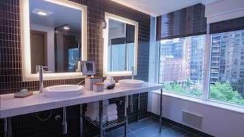 A modern bathroom with two sinks, large mirrors, and a view of a cityscape through a large window.
