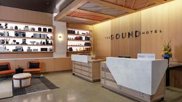 A hotel reception area with a modern design, featuring a reception desk, seating area, and a wall with shelves displaying various items.