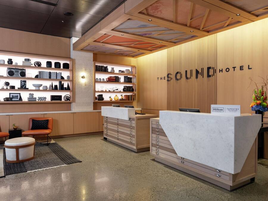 A hotel reception area with a modern design, featuring a reception desk, seating area, and a wall with shelves displaying various items.
