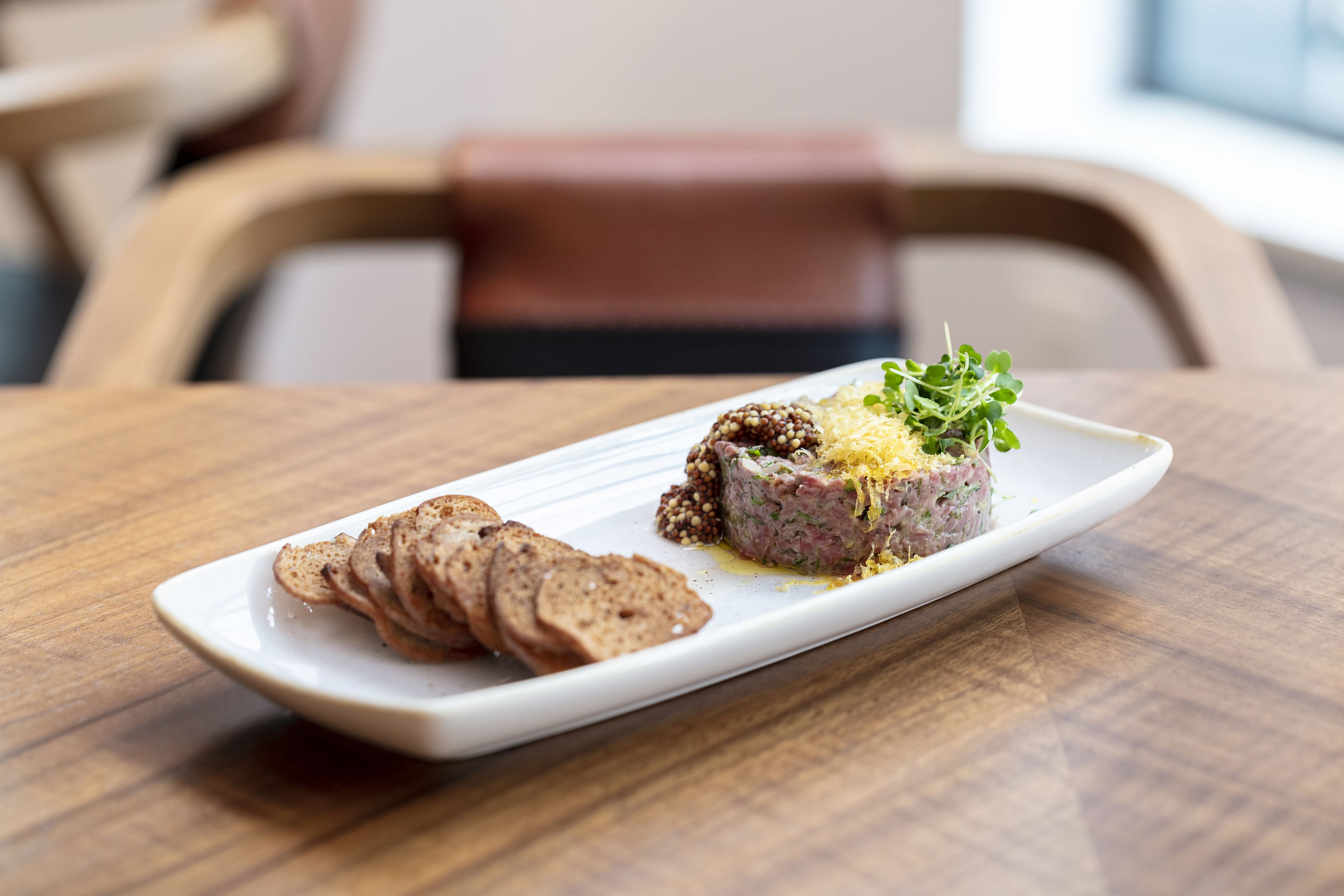 A white rectangular plate with a meat-based dish and sliced bread on a wooden table.
