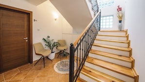 Una escalera con escalones de madera y barandillas negras, una puerta de madera, dos sillas, una mesita y una planta en maceta.