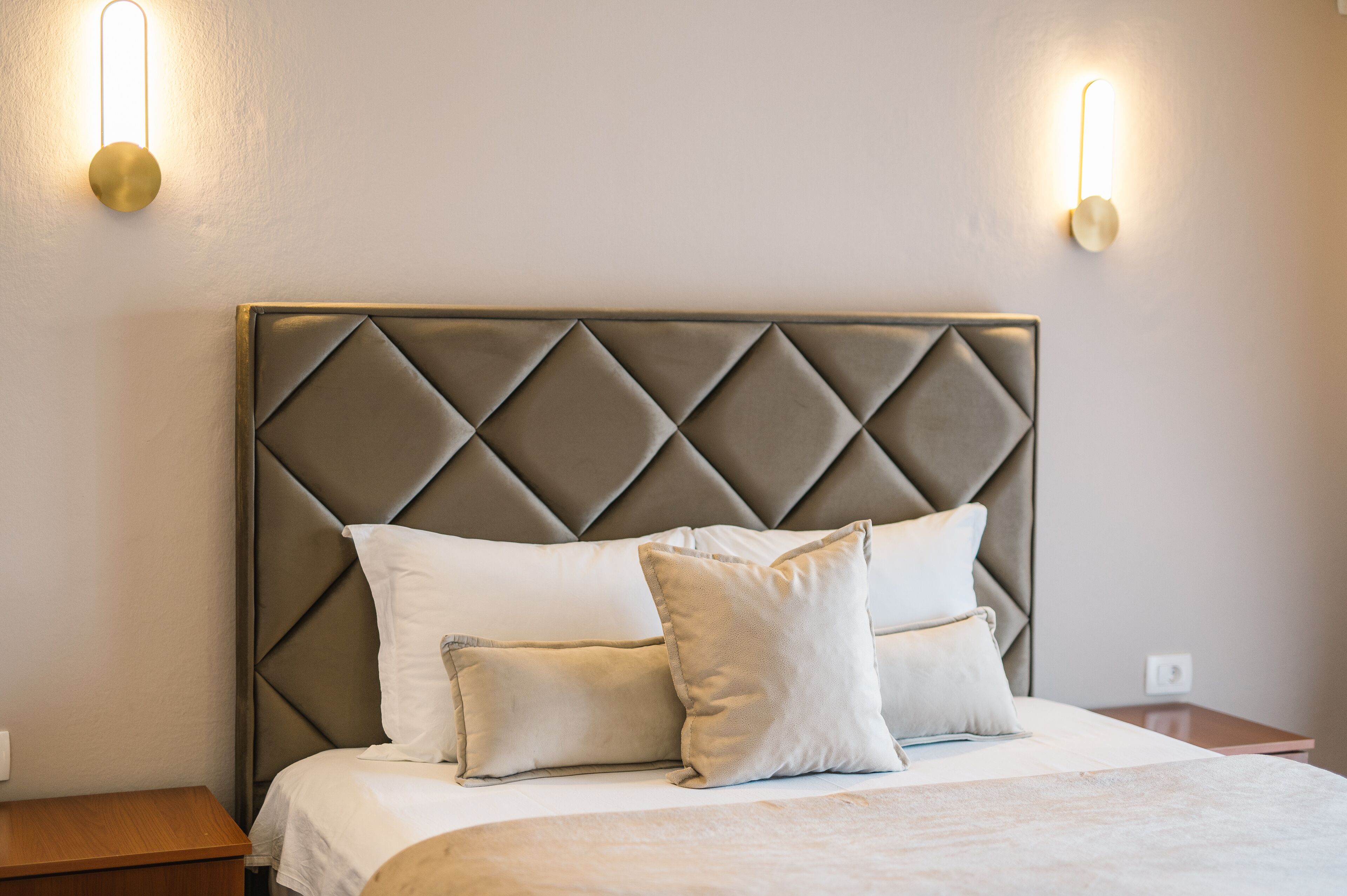 Un lit avec une tête de lit capitonnée, deux appliques murales et une table de chevet en bois.