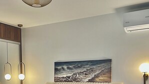 Un dormitorio con una cama, cabecera, un cuadro, una lámpara de pared y una mesita de noche.
