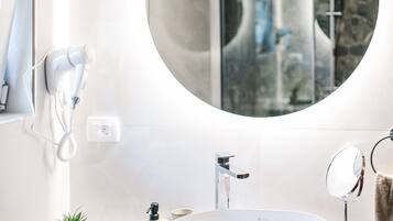 A modern bathroom with a large oval sink, a round mirror, a hairdryer, and a small potted plant.