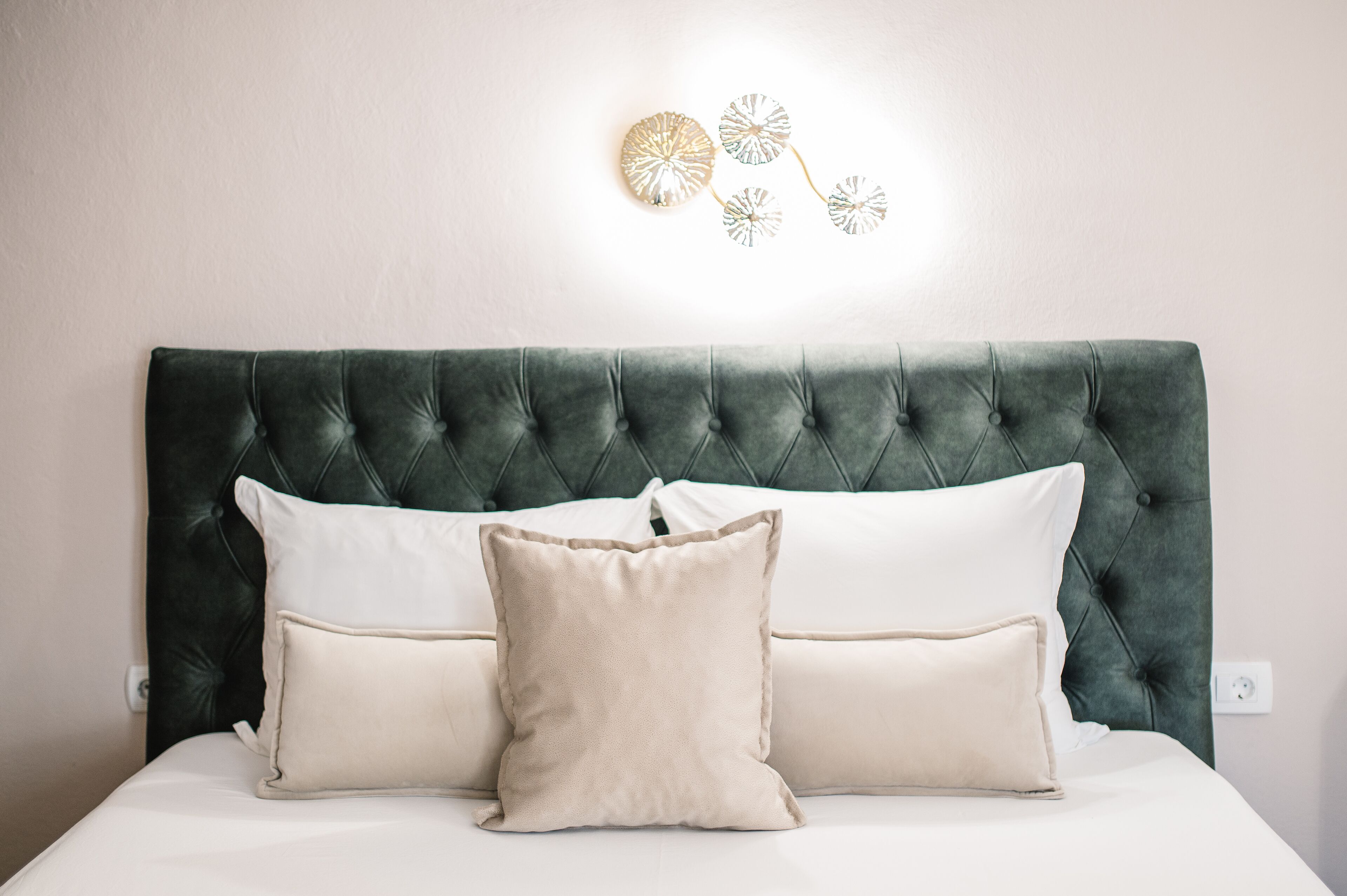 Un letto con testiera capitonné, due cuscini e una lampada a parete.
