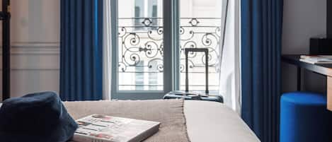 A hotel room with a bed, a suitcase, a pair of glasses, and a window with curtains.