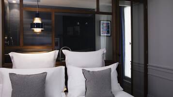 A hotel room with a bed, white pillows, a grey pillow, a hanging light fixture, and a window with curtains.