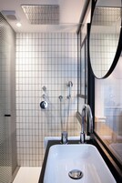 Une salle de bain moderne avec un mur recouvert de carreaux blancs, un grand miroir et un lavabo en chrome.